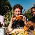 Three outdoor diners eating spiced chicken burger and sides