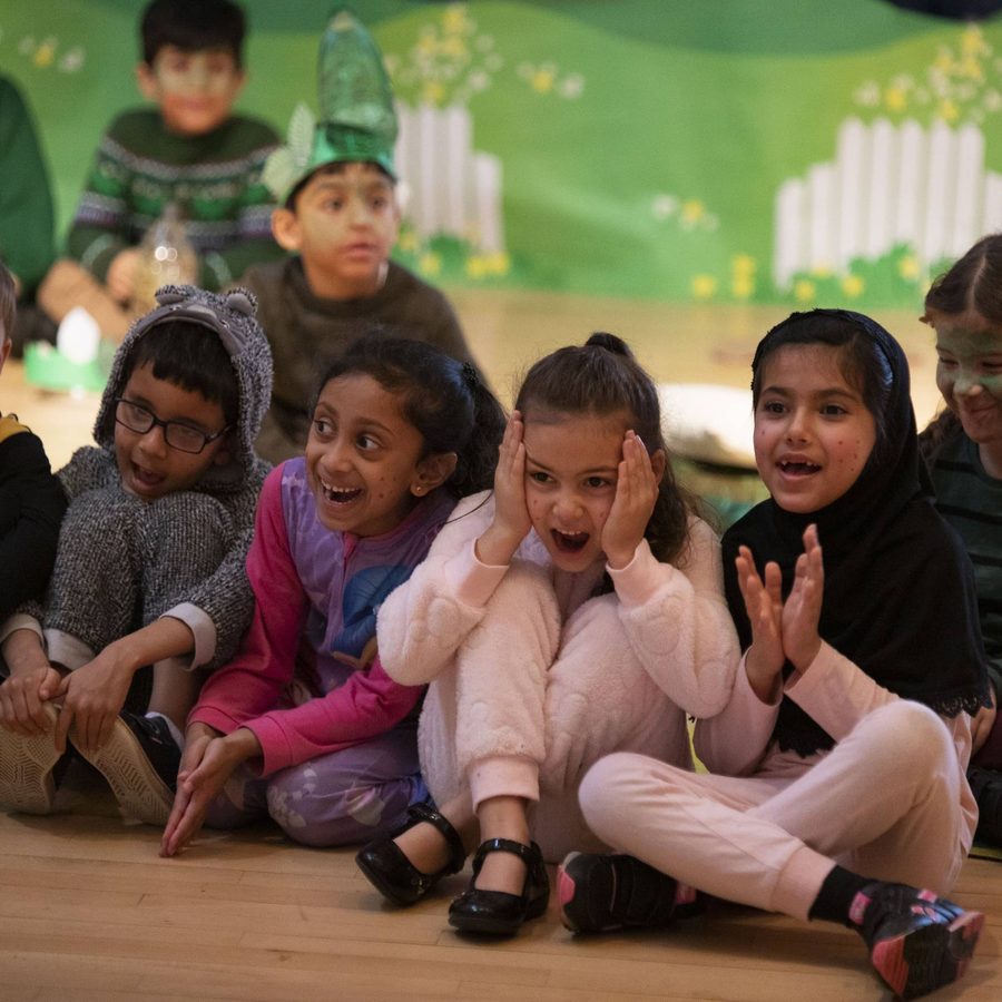 A row of primary children sitting on the floor in a row, smiling and laughing