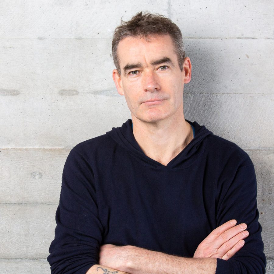 Rufus Norris stands next to the famous concreate walls of the national theatre.