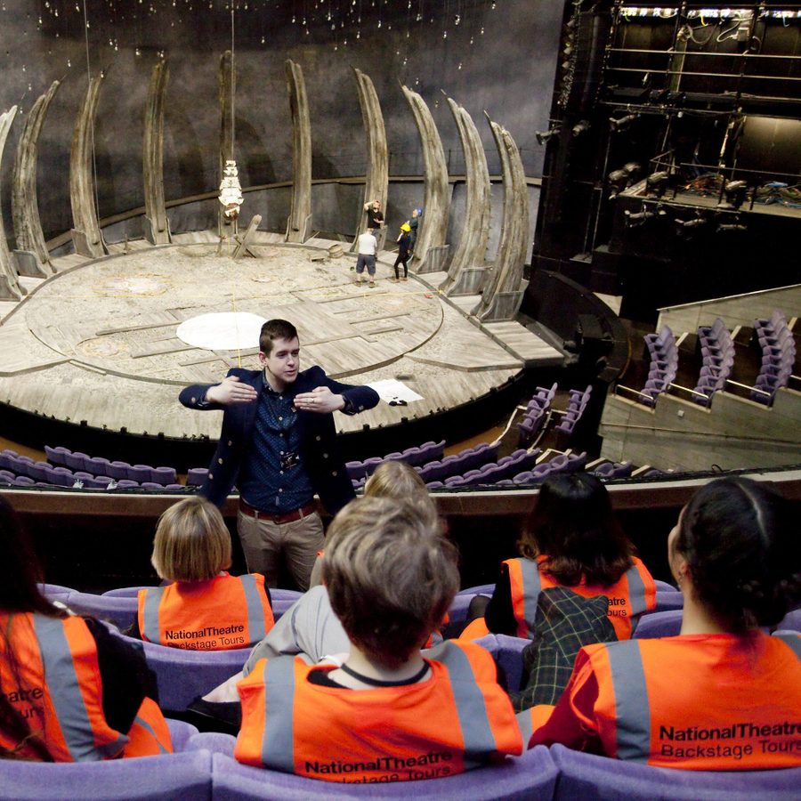 backstage-tour-march-2015-2000x1000-masthead-photo-ludo-des-cognets-sfw A tour guide talking to a tour group in the Olivier theatre auditorium. The tour participants wearing orange high-visibility vests.