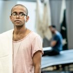 A man in a pink T-shit and glasses stands, looking into the distance.