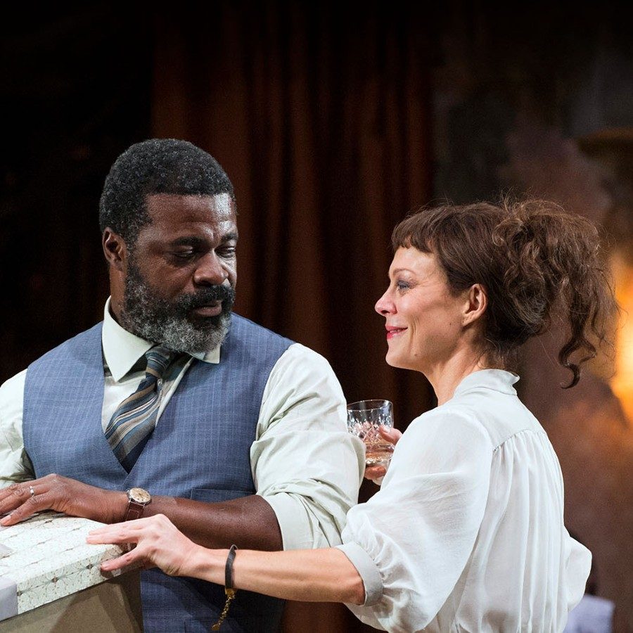 Helen McCrory and Danny Sapani in the National Theatre production of Medea, 2014. McCrory and Sapani are smiling and holding a large boxed gift.