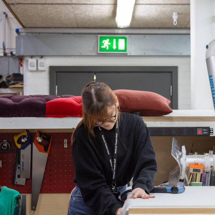 Props apprentice at workbench, holding fabric down