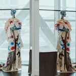 A dual-pane image showcases a mannequin adorned with a colorful, abstract costume against a backdrop of large windows and structural supports. The mannequin's outfit features bold splashes of blue, red, and other vibrant hues.