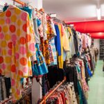 A colorful and well-organized aisle filled with a variety of clothing items neatly arranged on racks. On the left, there's a polka-dotted jacket prominently displayed. Other clothes in different colors and patterns are visible further down the aisle.