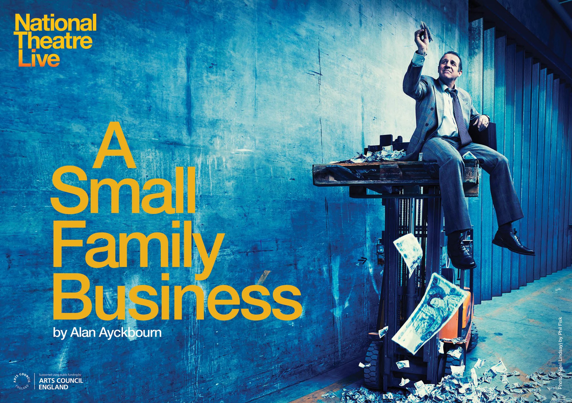 A man wearing a suit sits on a tall table and flies a paper aeroplane of money as money falls around him.