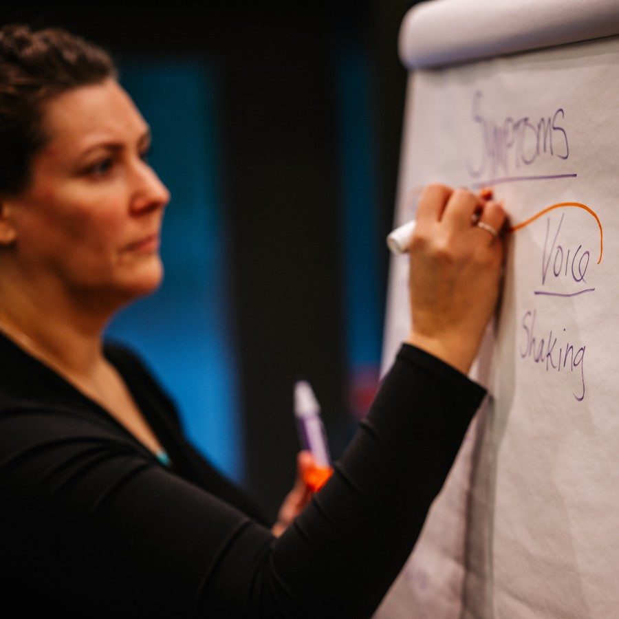 A person writes on a large notepad on an easel.