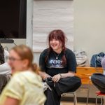 Four young adults sitting on chairs, engaged in a lively discussion in a rehearsal room.