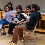 Four young people sitting and reading scripts in a rehearsal space.