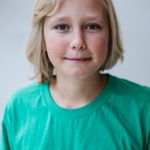 A young person with short blond hair is wearing a green T-shirt that has 