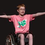 A young person in a wheelchair wearing glasses and a pink 