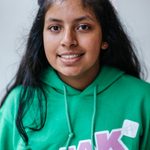 A person with long dark hair smiles at the camera, wearing a green hoodie with the words 